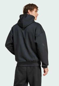 Sweatshirt preto com capuz, de corte solto, com bainha elástica e tecido ligeiramente texturizado. Apresenta ombros caídos e detalhes de design minimalistas.