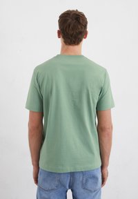 T-shirt in cotone verde con collo rotondo e maniche corte, caratterizzato da una trama liscia e una vestibilità rilassata, abbinato a jeans azzurri chiari.