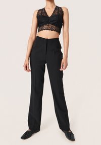 Top corto de encaje negro con patrón floral y escote en V, combinado con pantalones negros a medida con diseño de pierna recta y pliegues frontales.