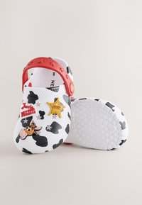 Beli natikači s črnimi kravjimi lisami, rdečim trakom z zvezdnim vzorcem in okraski s temo Igrače zgodba, vključno z Jessie, Bullseyem in šerifovo značko.