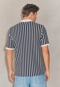 Gestreiftes Strick-Poloshirt in Marineblau und Creme, mit kurzen Ärmeln und Kragen. Die Textur wirkt gerippt, mit einer taillierten Passform.