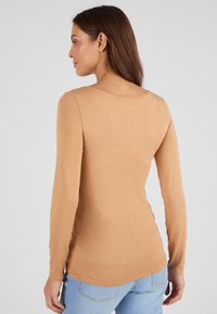 Maglia a maniche lunghe in morbido tessuto beige, con scollatura rotonda, silhouette aderente e orlo curvo, abbinata a jeans azzurri chiari.