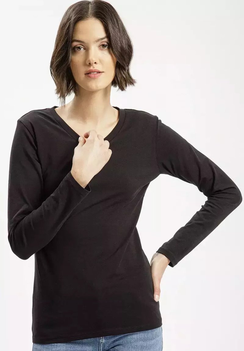 Czarna bluzka z długim rękawem i dekoltem w szpic, wykonana z gładkiego materiału, dopasowany krój i minimalne detale. Model pozujący z jedną ręką na piersi.