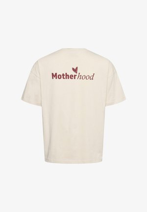 Beige t-shirt met de tekst "Moederschap" in rood en bruin, met een klein hartje boven de "h" op de achterkant in het midden.