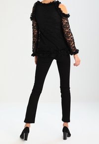 Svart spetsblus med volangärmar och nederkant, design med öppna axlar, i kombination med svarta åtsittande byxor och högklackade skor.