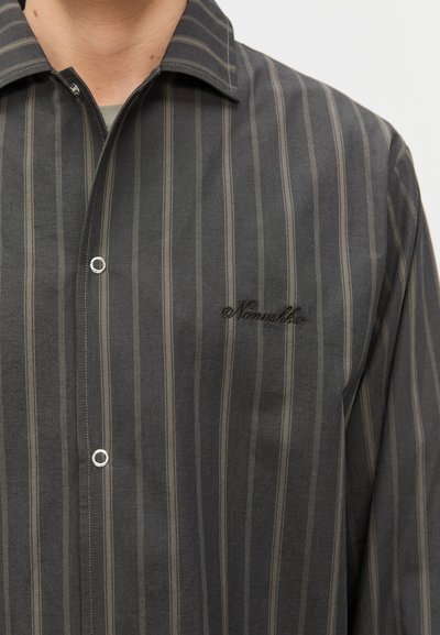Chemise à rayures gris foncé avec de fines rayures vertes et beiges, dotée d'un col pointu et d'un logo brodé sur la poitrine.