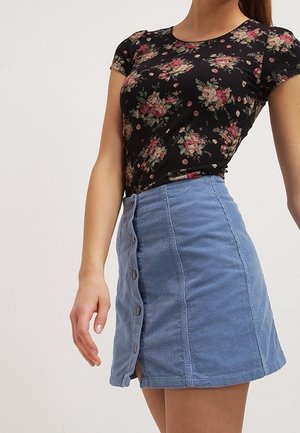 Musta kukkakuvioinen t-paita, jossa on lyhyet hihat, yhdistetty vaaleansiniseen velourminihelmaan, jossa on etunapit ja sivuhalkio.