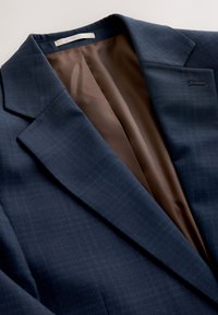 Dark blue suit jacket with subtle check pattern, showing brown inner lining and notch lapel collar.