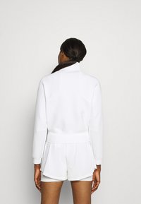 Hvid cropped sweatshirt med høj krave og lange ærmer, parret med hvide shorts. Glat stof, minimalistisk design, ingen synlige mønstre.