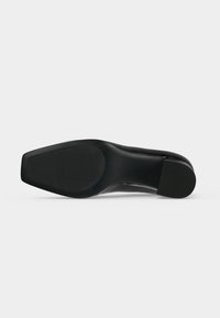 Semelle noire de chaussure formelle avec une forme d'orteil carrée et des zones de grip en caoutchouc texturé au talon et à la plante du pied.