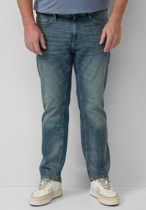 Hellblaue Denim-Jeans mit geradem Bein, subtilen Verwaschungen, fünf Taschen und Gürtelschlaufen, kombiniert mit weißen Sneakers.