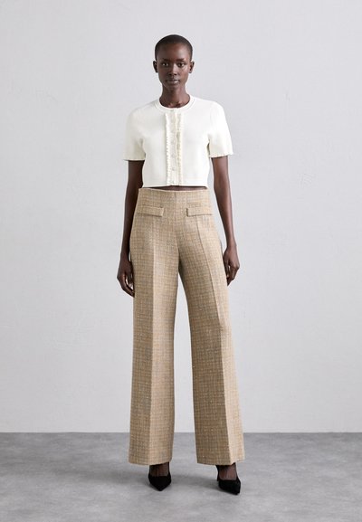 Elfenbensfarvet cropped striktop med korte ærmer og knapdetaljer, parret med brede tweedbukser i beige og guld, afsluttet med sorte hæle.