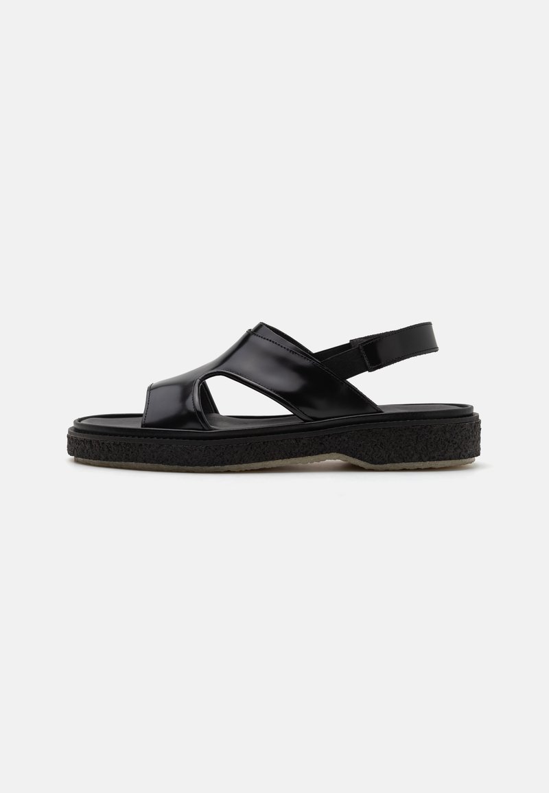 Black patent leather sandal with an open toe, side cutouts, and an adjustable strap. Textured black sole provides grip and comfort.