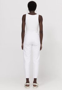Jeans blancos de cinturilla alta con un corte recto, dobladillos deshilachados y diseño clásico de cinco bolsillos. Llevados con una camiseta sin mangas blanca ajustada.