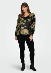 Maglietta a maniche lunghe con scollo a V in tessuto nero e oro con un motivo astratto e testurizzato, abbinata a pantaloni neri aderenti e stivaletti.