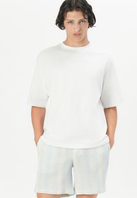 Camiseta de algodón blanca de manga corta combinada con pantalones cortos de patrón texturizado en azul claro. Diseño de corte holgado con un sencillo escote redondo.