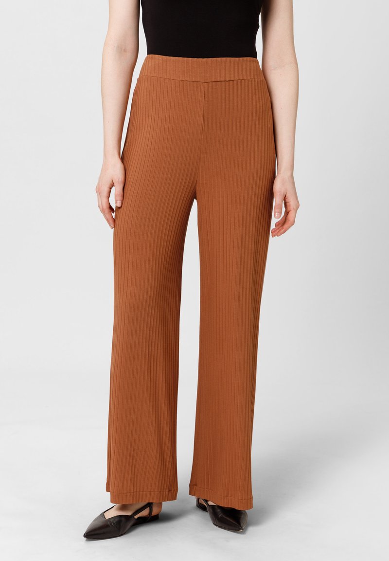 Roestkleurige wijde broek met ribbelstructuur en hoge tailleband, gecombineerd met zwarte puntige ballerina's.