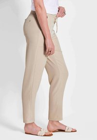 Beige instapbroek met een elastische tailleband, zijzakken en taps toelopende pijpen, gecombineerd met lichtgekleurde platte sandalen.