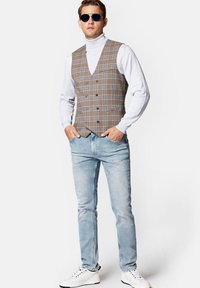 Brązowa kamizelka w kratę na szarym golfie, zestawiona z jasnoniebieskimi dżinsami. Białe sneakersy dopełniają stylizację. Posiada okulary przeciwsłoneczne i kieszenie.