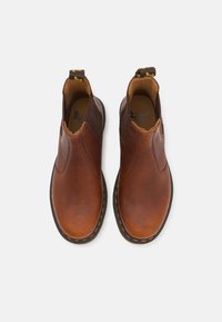 Braune Leder-Stiefeletten mit einer strukturierten Oberfläche, elastischen seitlichen Einsätzen und einer gelb gestickten Sohle. Verfügt über eine Zugschlaufe an der Rückseite.