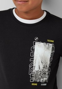 Zwarte sweatshirt met wit en gele grafische vormgeving met de woorden "TECHNO" en "SOUND", ronde halslijn met witte binnenafwerking, normale pasvorm.