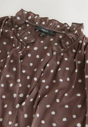 Braune Bluse mit weißen Punkten aus transparentem Stoff, mit gerafftem Ausschnitt und Schlitzöffnung, über das gesamte Kleidungsstück verteilt.