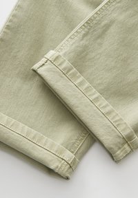 Pantalons en denim vert clair avec une texture douce, comportant des ourlets soigneusement repliés et des détails de couture visibles le long des bords.