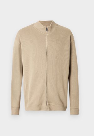Beiger Reißverschluss-Pullover mit hohem Kragen, gerippter Struktur und langen Ärmeln. Klare Linien und dezente Nahtdetails verleihen dem Design eine ansprechende Note.