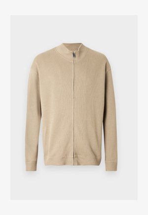 Suéter beige con cremallera, cuello alto, textura acanalada y mangas largas. Líneas limpias y detalles de costura sutiles realzan su diseño.