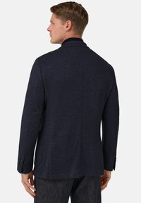 Námořnicky modré sako s rybí kostí vzorem, ostrým límcem, zapínáním na jeden knoflík a bočními kapsami; střih na míru, texturovaná tkanina.