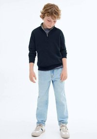 Marinblå fleece zip-up-tröja med en ljusgrå krage, kombinerad med ljusblå jeans och grå sneakers med mörka accenter.