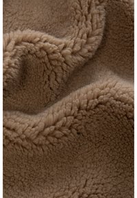 Pruunikas beežfliisriie, mille pehme ja tekstuuriga pind on kaetud pehme lainelise mustriga, luues sooja ja hubase välimuse.