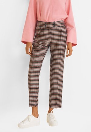Pantalons à carreaux avec une taille haute, présentant des motifs noirs et rouges, des détails de poches et une coupe fuselée, associés à des baskets blanches.