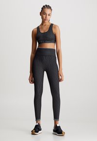Czarny strój sportowy składający się z prążkowanego biustonosza sportowego i legginsów z wysokim stanem, obydwa z logo Calvin Klein, zestawiony z czarnymi sneakersami.