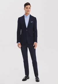 Granatowy garnitur o dopasowanym kroju; jednorzędowa marynarka i slim fit spodnie. Jasnoniebieska koszula i poszetka, wykończone czarnymi loafersami.