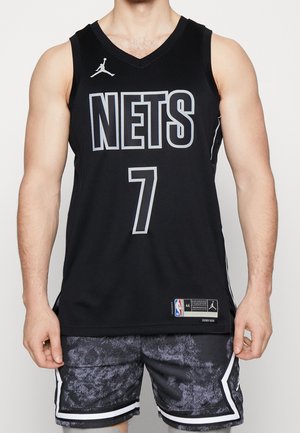 Mężczyzna ubrany w czarną koszulkę do koszykówki Brooklyn Nets z numerem 7 i pasujące czarne krótkie spodenki w wzory, stojący na jednolitym tle.