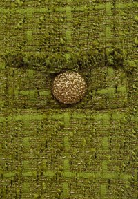 Tejido texturizado verde con un patrón tejido, que presenta un botón decorativo dorado. La superficie tiene una apariencia ligeramente difusa y en capas.