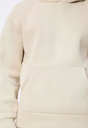 Sweat à capuche beige en tissu doux. Comprend une poche kangourou frontale et des poignets et ourlet côtelés. Texture lisse et mate.