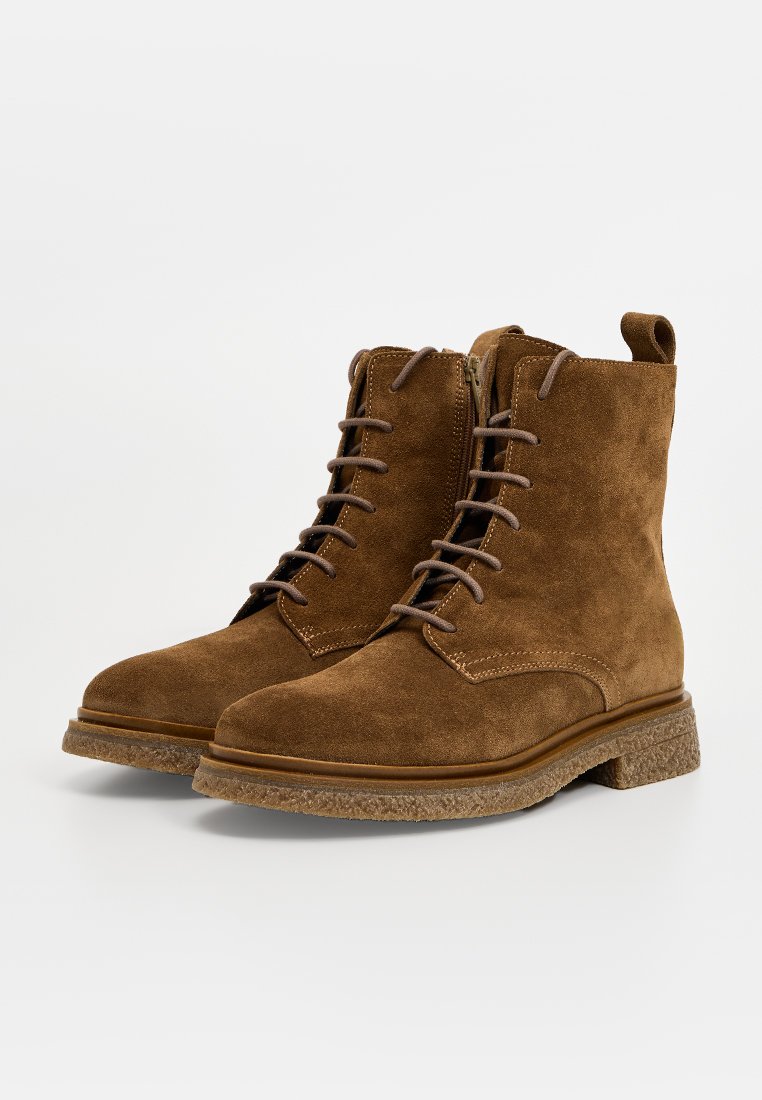 Braune Wildleder Schnürstiefeletten mit seitlichem Reißverschluss und strukturierten Gummisohle, gezeigt vor einem schlichten weißen Hintergrund.