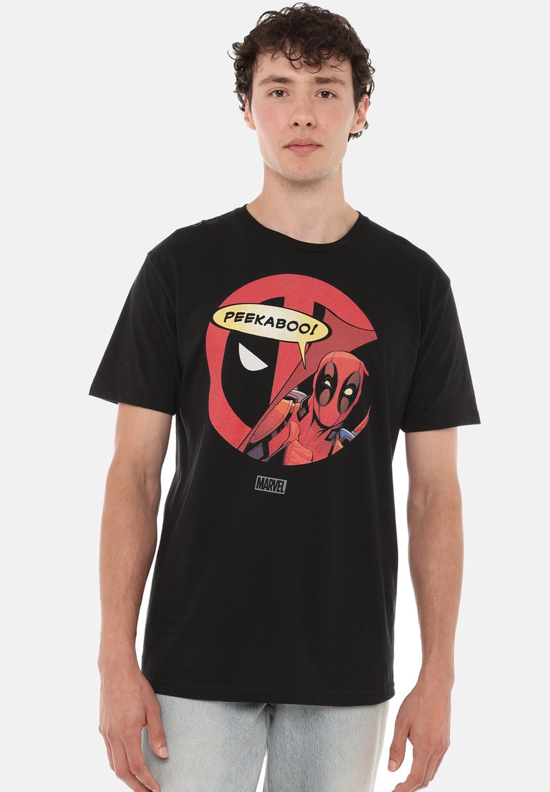 Young man wearing a black Marvel Deadpool t-shirt with Deadpool character and speech bubble saying "Peekaboo!" on front, paired with light jeans.