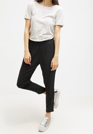 Zwarte taps toelopende broek, zachte stof, met een elastische tailleband. Gecombineerd met een gestreept T-shirt met korte mouwen en lichtgrijze sneakers.