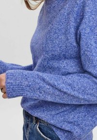 Blauer gestrickter Pullover mit strukturiertem Finish, langen gerippten Ärmeln und rundem Ausschnitt, getragen über Jeans.