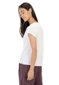 Weißes T-Shirt mit kurzen Ärmeln, Rundhalsausschnitt und lockerer Passform. Weiches Material, dezente Textur und ein kleiner Markenaufnäher am Saum.