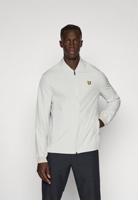 Light gray bomber jacket with a zip front, elastic cuffs, and side pockets. Features a small yellow logo on the chest.