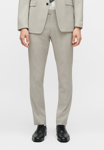Ανοιχτό γκρι παντελόνι κοστουμιού σε εφαρμοστή γραμμή, κατασκευασμένο από λείο ύφασμα. Διαθέτει επίπεδη εμπρόσθια σχεδίαση και κομψές πλαϊνές τσέπες. Συνδυασμένο με μαύρα παπούτσια.