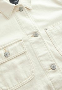 Cream-colored corduroy shirt with a button-up collar, featuring two front pockets, silver hardware buttons, and textured fabric.