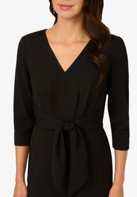 Schwarzes Kleid mit Dreiviertelärmeln, einem V-Ausschnitt und einem gebundenen Gürtel in der Taille. Glatte Textur und taillierte Silhouette.
