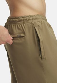 Hnedé športové nohavice s elastickým pásom, bočnými zipsovými vreckami a decentnou logom nášivkou. Hladký materiál a priliehavý strih pre pohodlie.