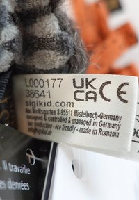 Gray plush fabric labeled with care instructions; shows textures, design details, and a tag indicating eco-friendly materials and origin.