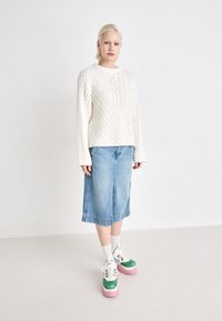 Hvit kabelstrikket genser med rund hals, kombinert med en lyseblå denim midi-skjørt. Fottøyet har grønn glitter og rosa såler.